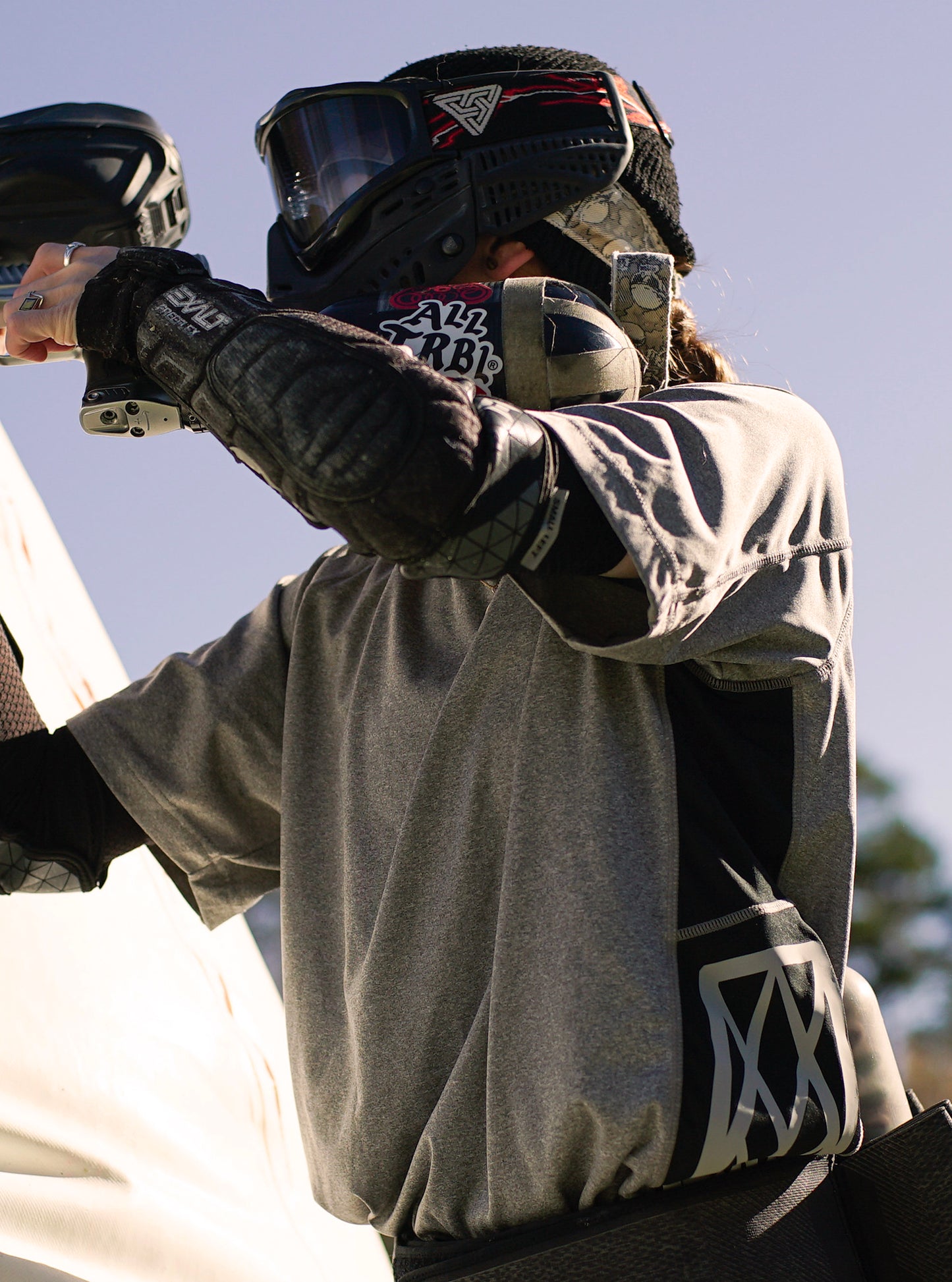 Person in paintball gear holding a gun with a clear sky background